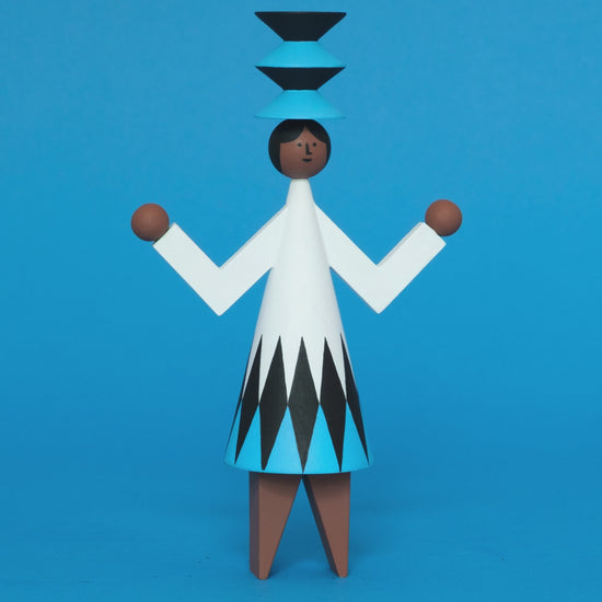 A spinning video of a colourful wooden sculpture with a black, white and blue diamond patterned dress with brown legs and a matching blue and black headdress on a plain blue background.