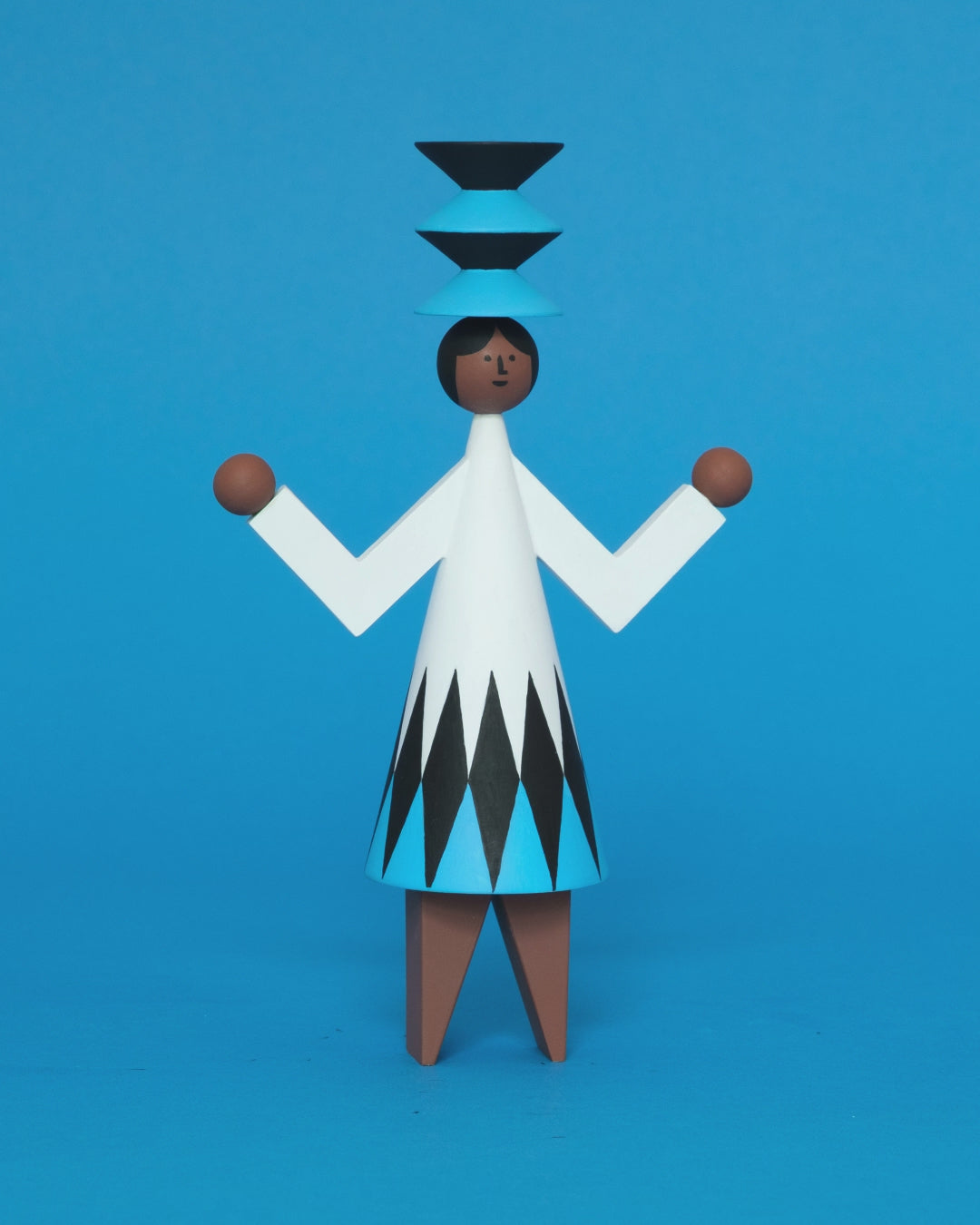 A spinning video of a colourful wooden sculpture with a black, white and blue diamond patterned dress with brown legs and a matching blue and black headdress on a plain blue background.