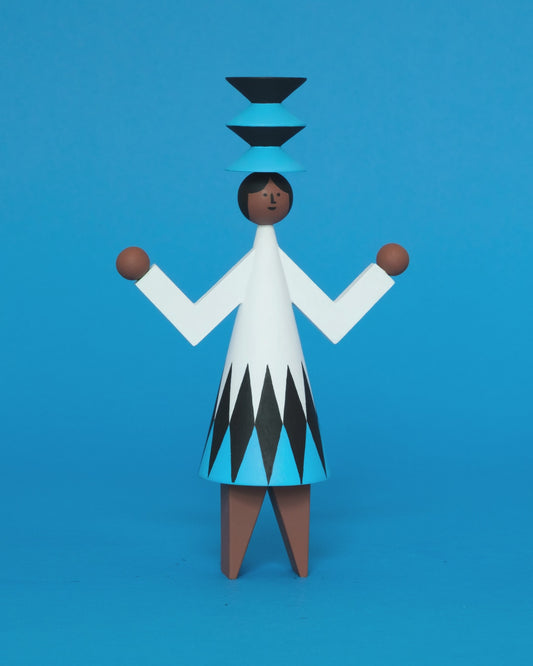 A spinning video of a colourful wooden sculpture with a black, white and blue diamond patterned dress with brown legs and a matching blue and black headdress on a plain blue background.