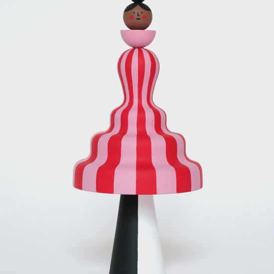 A video of a colourful sculpture with a pink and red stripey body with white and black legs on a plain white background.