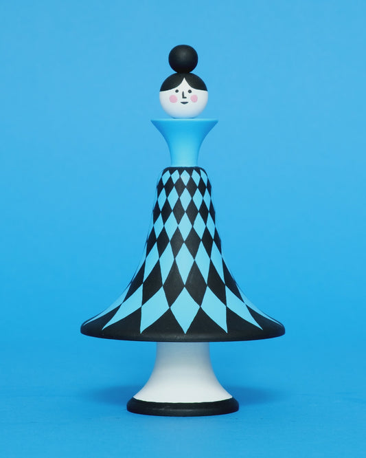 A spinning video of a colourful wooden sculpture with a black and blue diamond patterned curved body with white legs on a plain blue background.