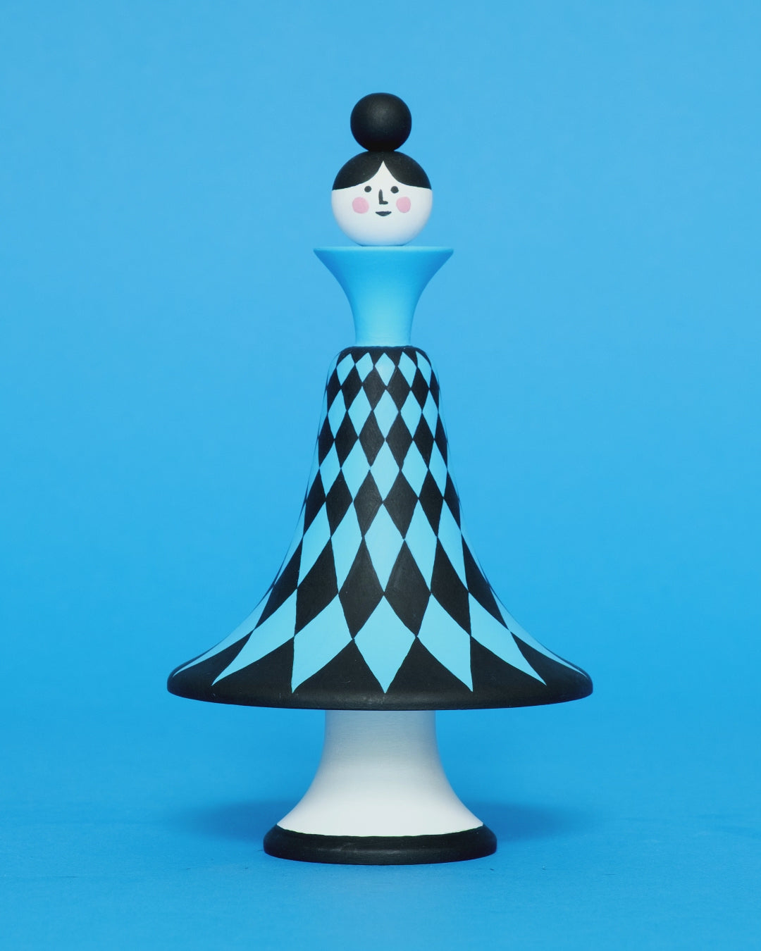 A spinning video of a colourful wooden sculpture with a black and blue diamond patterned curved body with white legs on a plain blue background.
