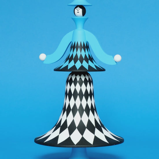 A spinning video of a colourful sculpture with a white, black and blue diamond patterned curved body with blue legs and a blue top hat on a plain blue background.
