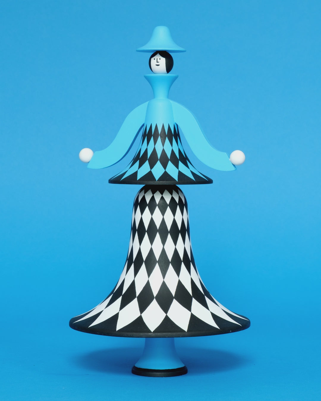 A spinning video of a colourful sculpture with a white, black and blue diamond patterned curved body with blue legs and a blue top hat on a plain blue background.