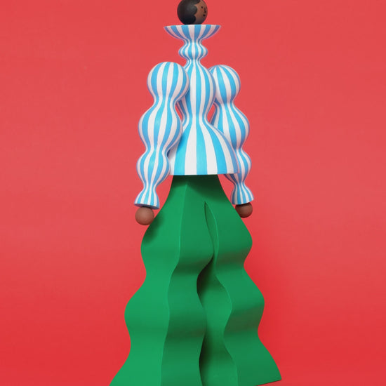 A video of a colourful sculpture with a blue and white stripey body with wavy green trousers on a plain orange background.