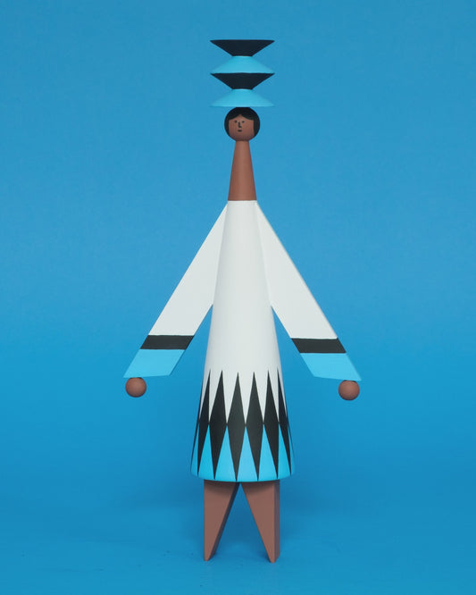 A spinning video of a colourful wooden sculpture with a black, white and blue diamond patterned dress with brown legs and a matching blue and black headdress on a plain blue background.