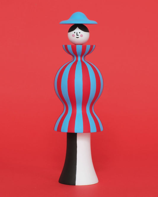 A spinning video of a colourful sculpture of a figure made from a red and blue stripey body with white and black legs with a blue hat on a plain orange background.