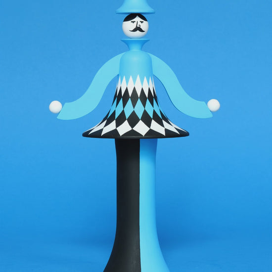 A spinning video of a colourful sculpture with a white, black and blue diamond patterned curved body with blue and black legs and a blue top hat on a plain blue background.