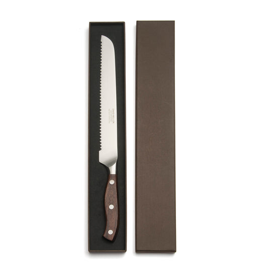 A serrated bread knife with a stainless steel blade and a wooden handle, displayed in an elegant dark box. The box is partially open, revealing the knife's polished surface and the craftsmanship of the handle.