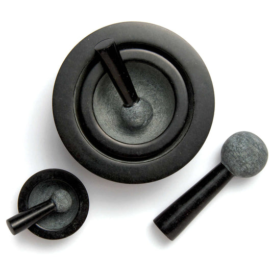 A set of three black stone mortars and pestles of varying sizes. The largest mortar features a wide bowl and a tall pestle, while the smaller ones have a more compact design. The smooth surfaces contrast with the textured pestle ends.