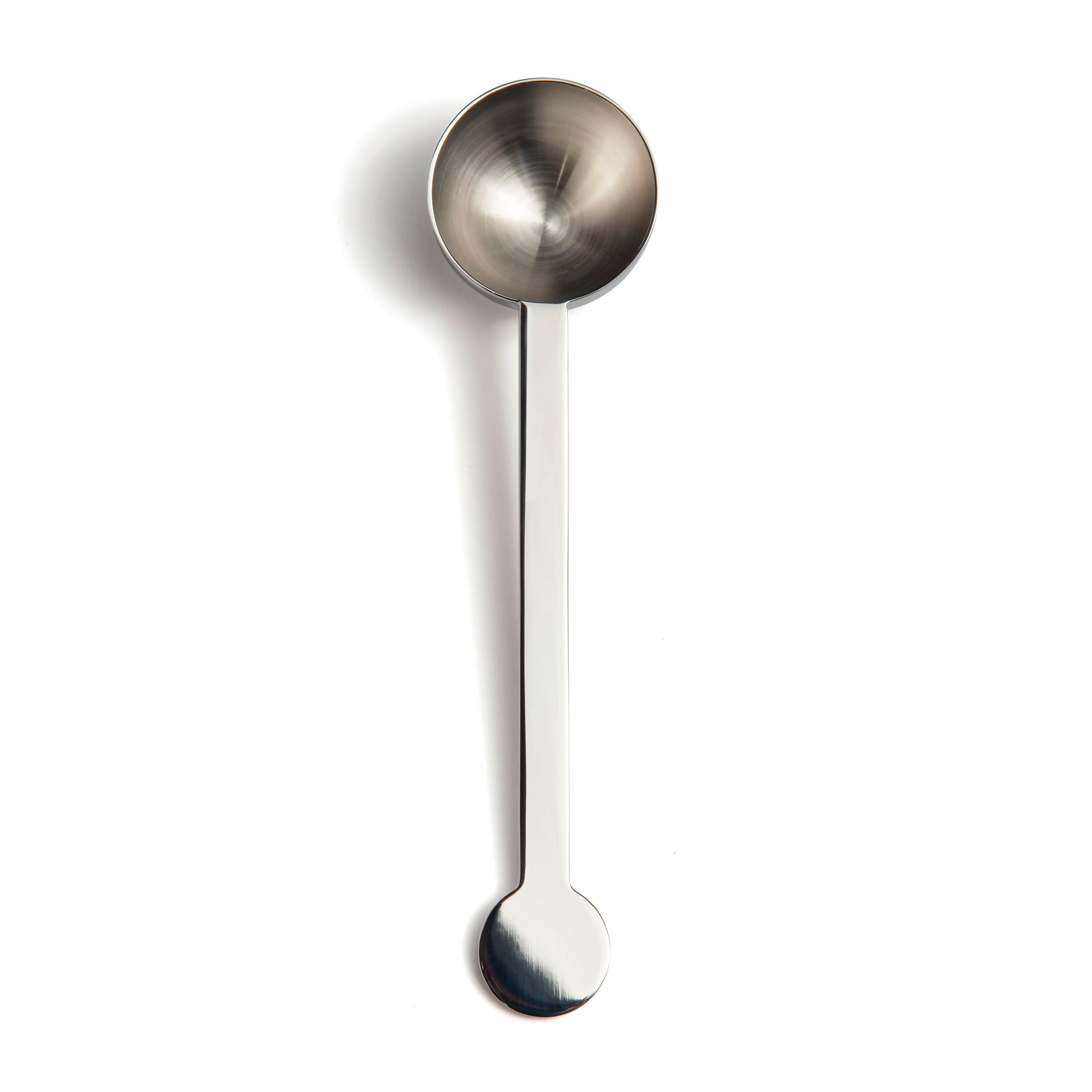 A stainless steel measuring spoon with a round bowl and a long handle, positioned vertically against a plain white background. The spoon has a polished finish, reflecting light subtly.