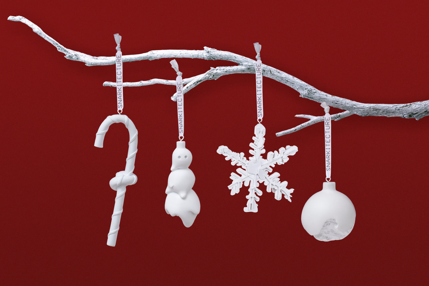 Four white Christmas ornaments hang from a silver branch against a deep red background. The ornaments include a candy cane, a snowman, a snowflake, and a round bauble, all featuring a minimalist design.