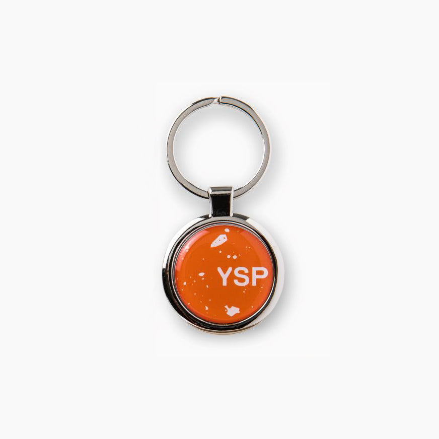 A round keyring featuring a bright orange background with the letters "YSP" prominently displayed in white. 